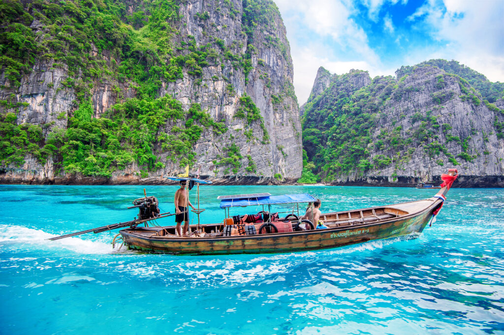Traditional long-tail boat sailing in crystal-clear waters near limestone cliffs in Thailand